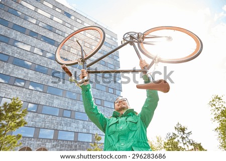 people, sport, style, leisure and lifestyle - happy young hipster man rising up and holding fixed gear bike s in city