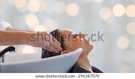 beauty salon, hair care and people concept - hairdresser hands washing happy young woman head over holidays lights background