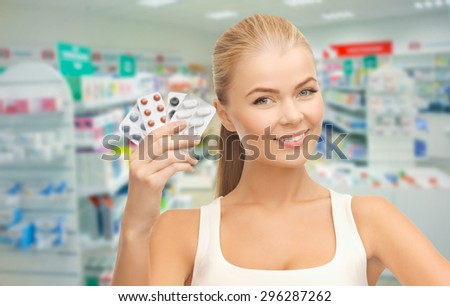 medicine, pharmacy, people, health care and pharmacology concept - happy young woman with variety of pills over drugstore background