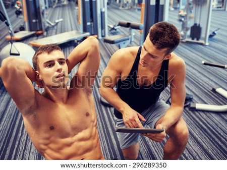 sport, fitness, lifestyle, technology and people concept - man and personal trainer with tablet pc computer and flexing abdominal muscles in gym