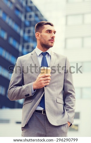 business, hot drinks and people and concept - young serious businessman with paper coffee cup over office building