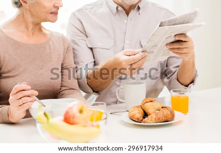 family, mass media, news and people concept - close up of happy senior couple having breakfast and reading newspaper at home