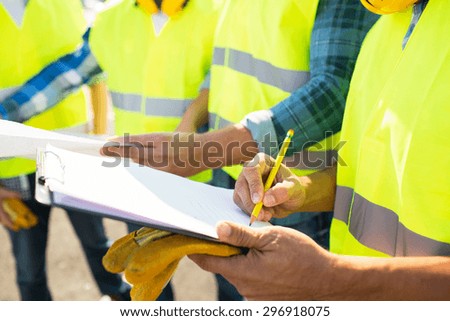 industry, building, paperwork and people concept - close up of builders in high visible vests writing to clipboard