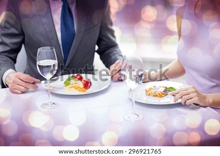 restaurant, food, people, date and holiday concept - close up of couple eating appetizers at restaurant over violet holidays lights background