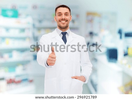 medicine, pharmacy, people, health care and pharmacology concept - smiling male pharmacist in white coat showing thumbs up over drugstore background