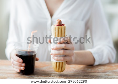 fast food, people and unhealthy eating concept - close up of woman hands with hot dog and  drink sitting at table