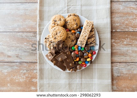 junk food, sweets and unhealthy eating concept - close up of candies, chocolate, muesli and cookies on plate