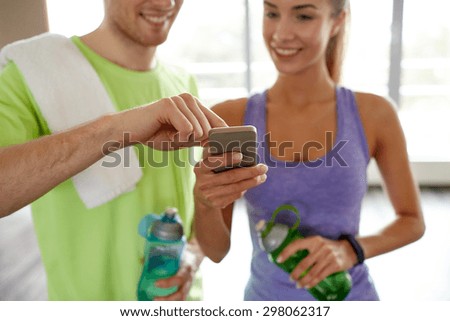 fitness, sport, technology and slimming concept - close up of smiling young woman and personal trainer with smartphone and water bottles in gym