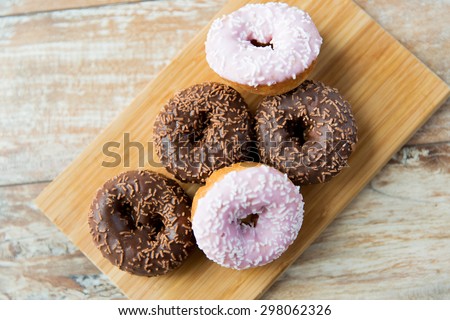 food, junk-food and eating concept - close up of glazed donuts on wooden board
