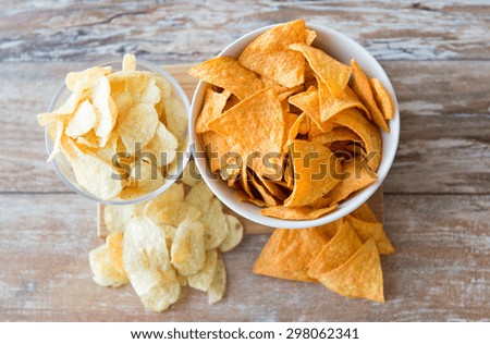 fast food, junk-food, cuisine and eating concept - close up of potato crisps and corn nachos in bowls on table
