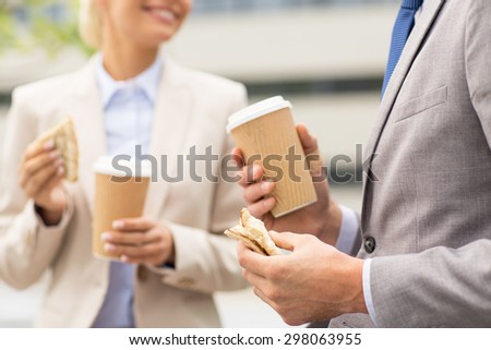 business, food, drink, communication and people concept - close up of smiling businessmen with coffee cups and sandwiches having lunch and talking outdoors