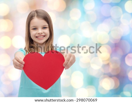 love, happiness, charity, children and people concept - smiling little girl giving red heart over blue holidays lights background
