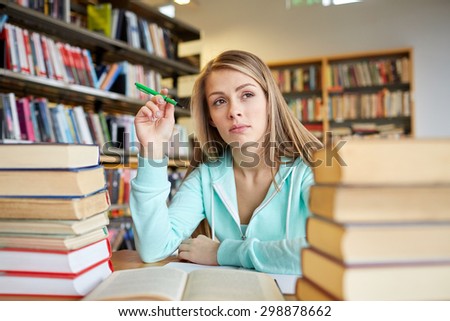 people, knowledge, education, literature and school concept - bored student girl or young woman with books dreaming in library