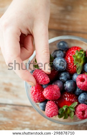 healthy eating, dieting, vegetarian food and people concept - close up of woman hands with berries mix in glass bowl on wooden table