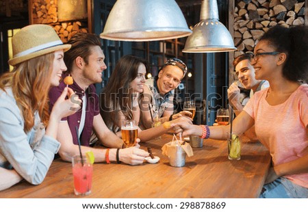people, leisure, friendship and communication concept - group of happy smiling friends drinking beer and cocktails eating and talking at bar or pub