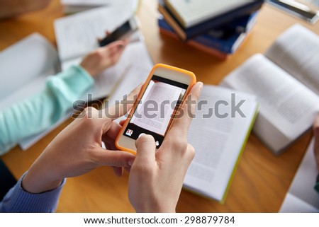 people, education, technology and exam concept - close up of students with smartphones taking picture of books page and making cheat sheet in school library