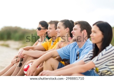 summer holidays, sport, leisure and people concept - group of happy friends sitting on beach with ball