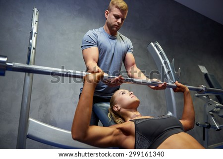sport, fitness, teamwork, bodybuilding and people concept - young woman and personal trainer with barbell flexing muscles in gym
