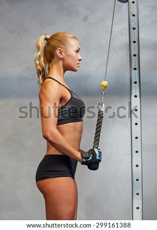 sport, fitness, lifestyle and people concept - young woman flexing muscles on cable gym machine