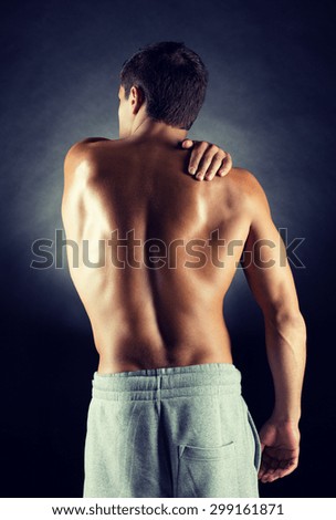 pain relief, sport, bodybuilding, strength and people concept - young man standing over black background