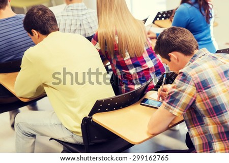 education, high school, technology and people concept - group of students writing test and social networking on smartphone in classroom