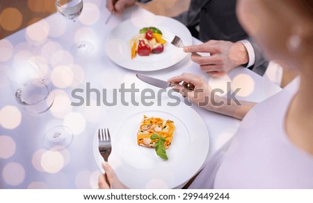 restaurant, food, people, date and holiday concept - close up of couple eating appetizers at restaurant over holidays lights background