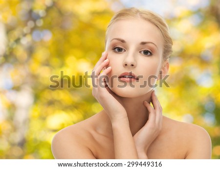 beauty, people and body care concept - beautiful young woman touching her face over yellow autumn background