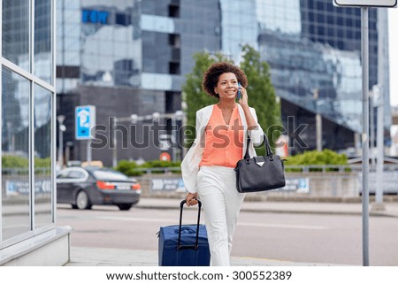 travel, business trip, people and technology concept - happy young african american woman with travel bag walking down city street and calling on smartphone