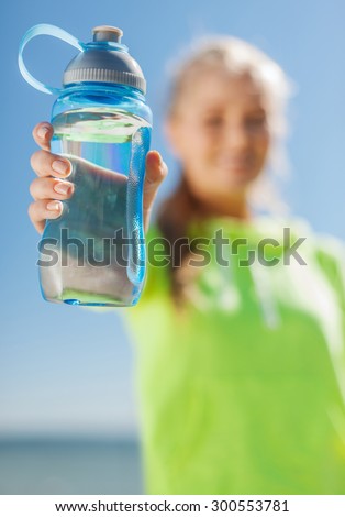 sport, fitness, exercise, nutrition and lifestyle concept - woman showing a bottle of water after doing sports outdoors