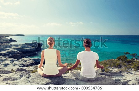 fitness, yoga, people and lifestyle concept - couple meditating on beach from back