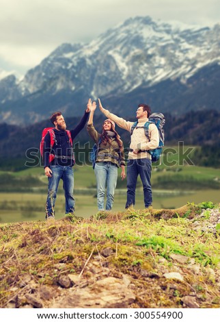 adventure, travel, tourism, hike and people concept - group of smiling friends with backpacks making high five gesture over mountains background