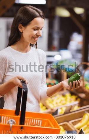 sale, shopping, consumerism and people concept - happy young woman with food basket holding cucumber in market