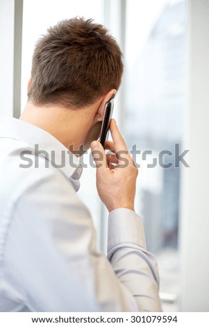 business, technology and people concept - businessman calling on smartphone and looking out office window