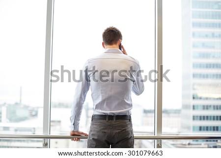 business, technology and people concept - businessman calling on smartphone and looking out office window