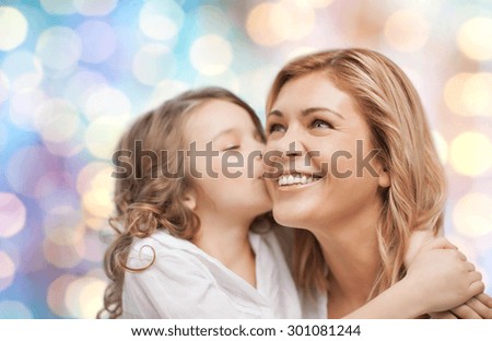 people, motherhood, family and adoption concept - happy mother and daughter hugging and kissing over blue holidays lights background