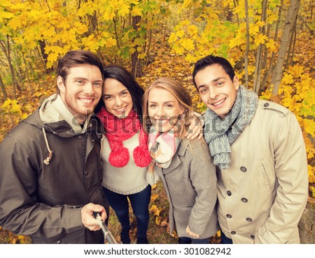 season, people, technology and friendship concept - group of smiling friends with smartphone or digital camera and selfie stick taking picture in autumn park