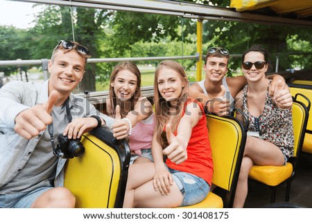 friendship, travel, vacation, summer and people concept - group of happy friends with digital camera traveling by tour bus and showing thumbs up