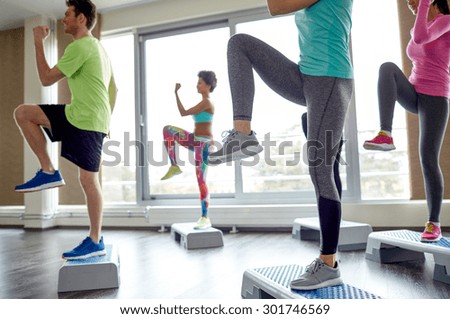 fitness, sport, aerobics and people concept - group of smiling people working out and raising legs on step platforms in gym
