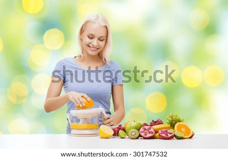 healthy eating, vegetarian food, diet, detox and people concept - smiling woman with squeezer squeezing fruit juice over summer green holidays lights background