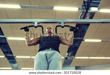 sport, fitness, lifestyle and people concept - young man doing pull-ups in gym