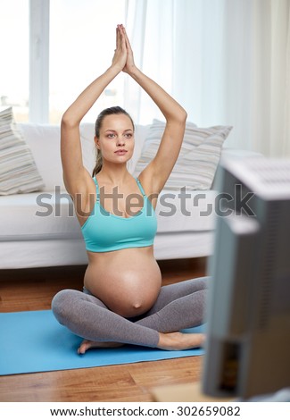 pregnancy, sport, yoga, people and healthy lifestyle concept - happy pregnant woman meditating and watching tv at home