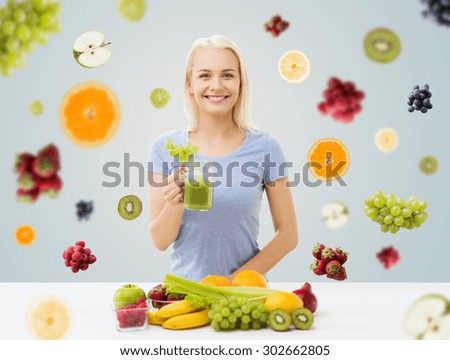 healthy eating, vegetarian food, diet, detox and people concept - smiling woman drinking green vegetable juice or shake from glass over fruits and berries on gray background