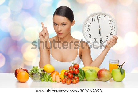 people, eating and diet concept - woman with healthy food holding big clock, pointing finger up and warning over blue lights background