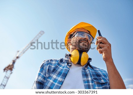 industry, building, technology and people concept - male builder in hardhat with walkie talkie or radio outdoors
