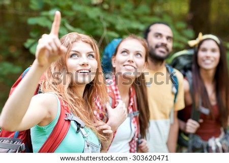 adventure, travel, tourism, hike and people concept - group of smiling friends with backpacks pointing finger in woods