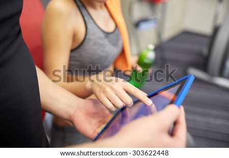 sport, fitness, lifestyle, technology and people concept - close up of trainer hands with tablet pc computer and woman working out in gym