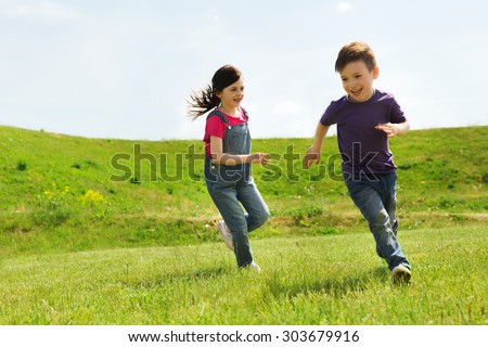 summer, childhood, leisure and people concept - happy little boy and girl playing tag game and running outdoors on green field