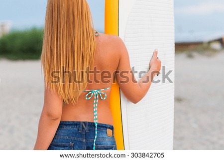 sea, summer vacation, water sport and people concept - woman with surfboard on beach from back