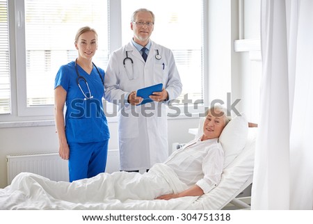 medicine, age, health care and people concept - doctor and nurse with tablet pc computer visiting senior patient woman at hospital ward