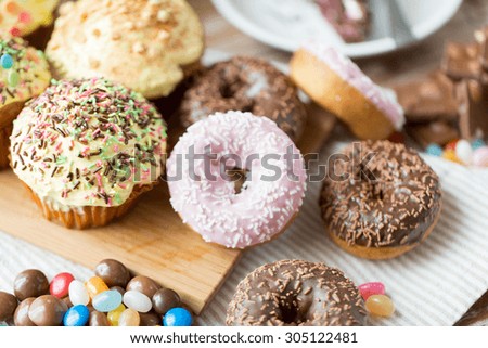 sweet food, junk-food and eating concept - close up of glazed donuts, candies and muffins on wooden board